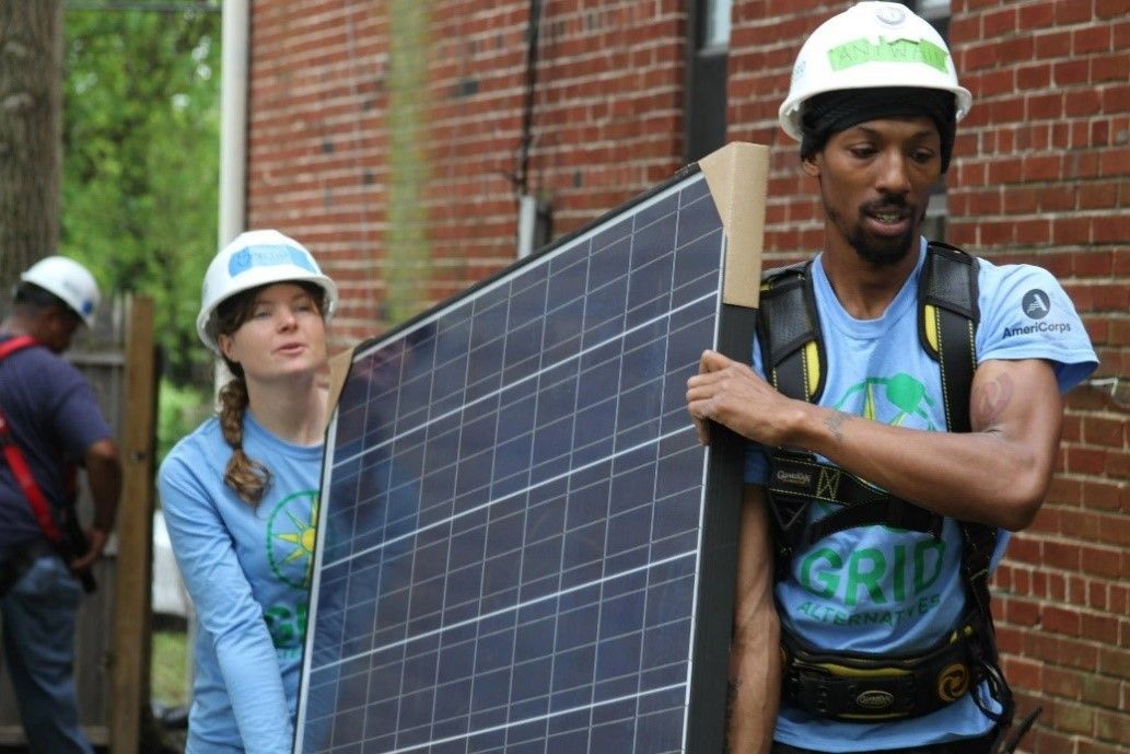 Two Americorps members carry a solar panel for installation.